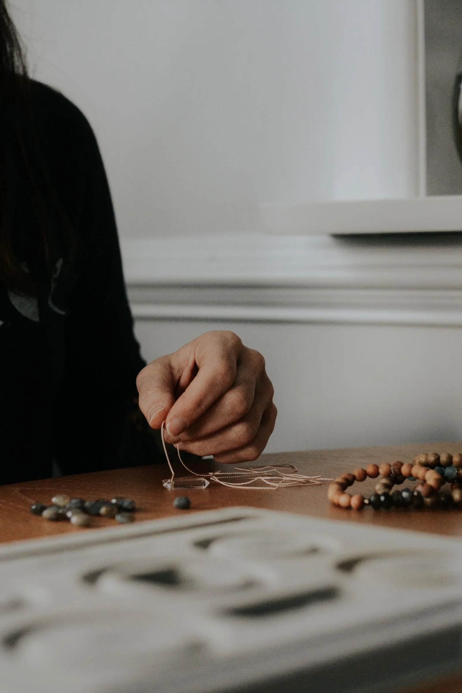 A woman making a quartz crystal and wood bead bracelet at her kitchen table. 