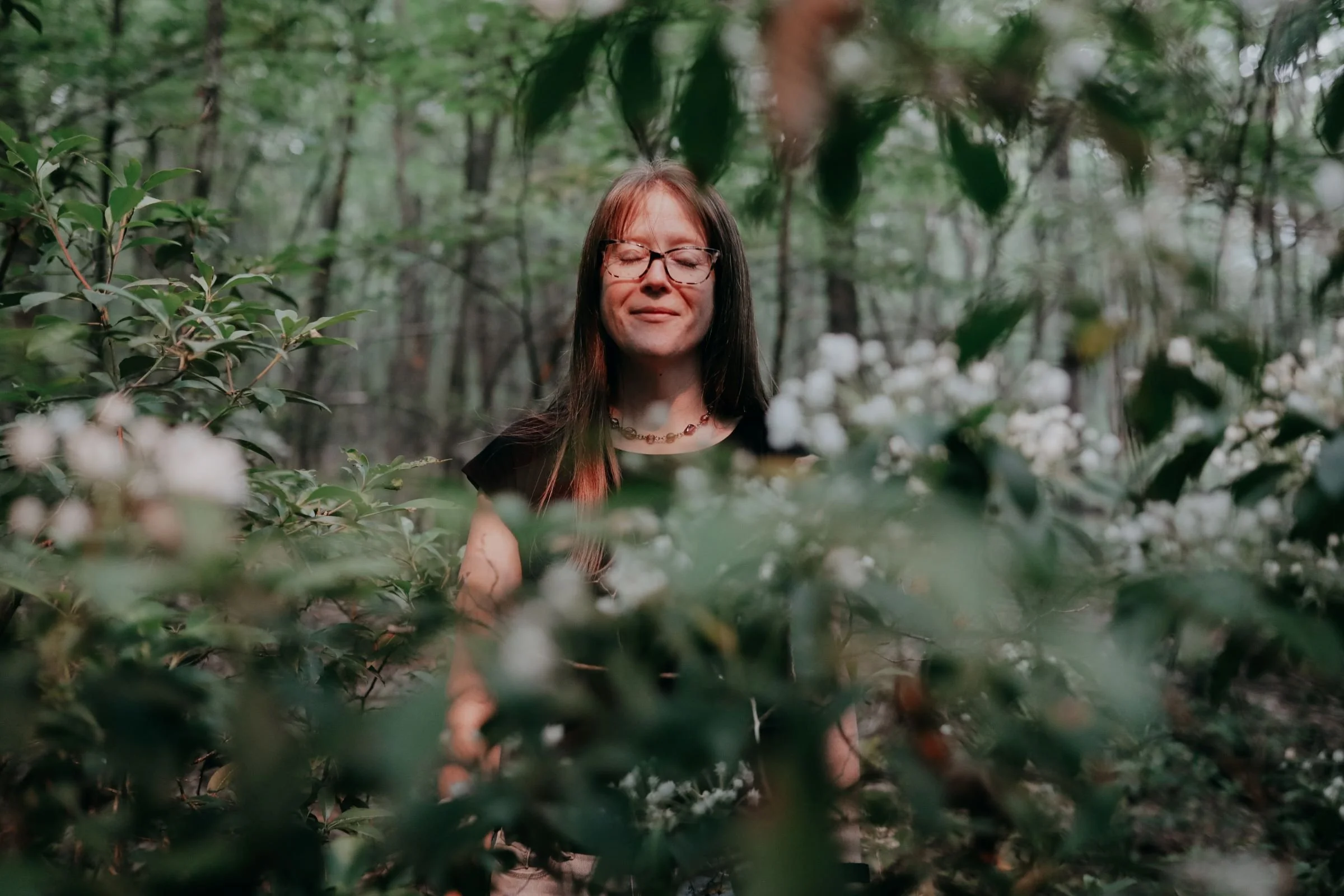 a woman standing in the woods surrounded by mountain laurel