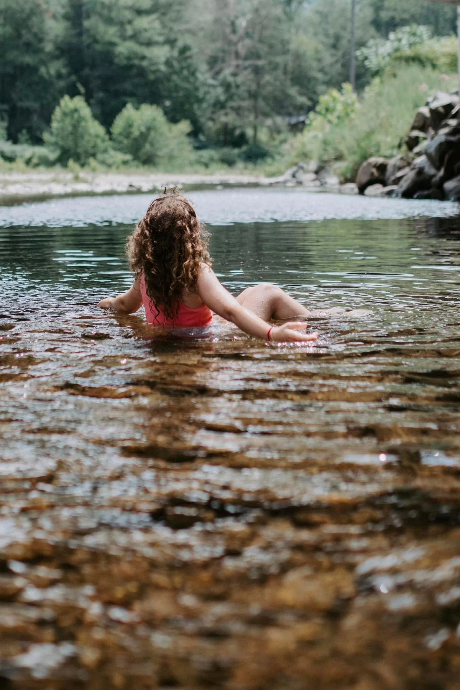 little girl with brown, curly hair, sitting in the Loyalsock creek, looking at the forest