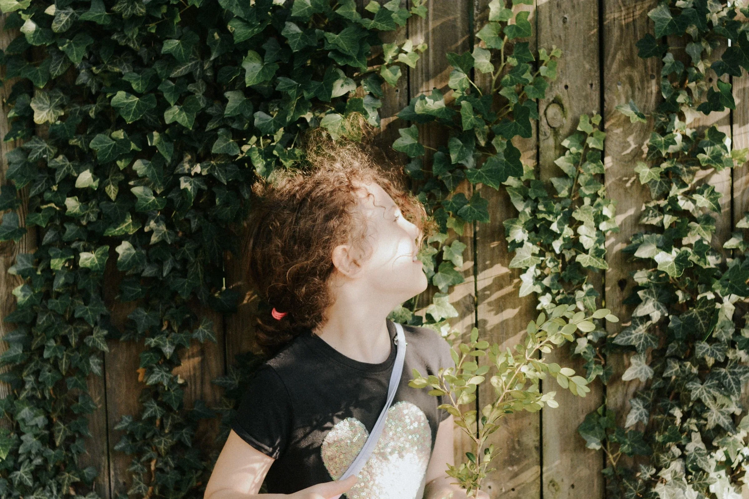a little girl stands in front of an ivy covered wood fence in Williamsport, PA