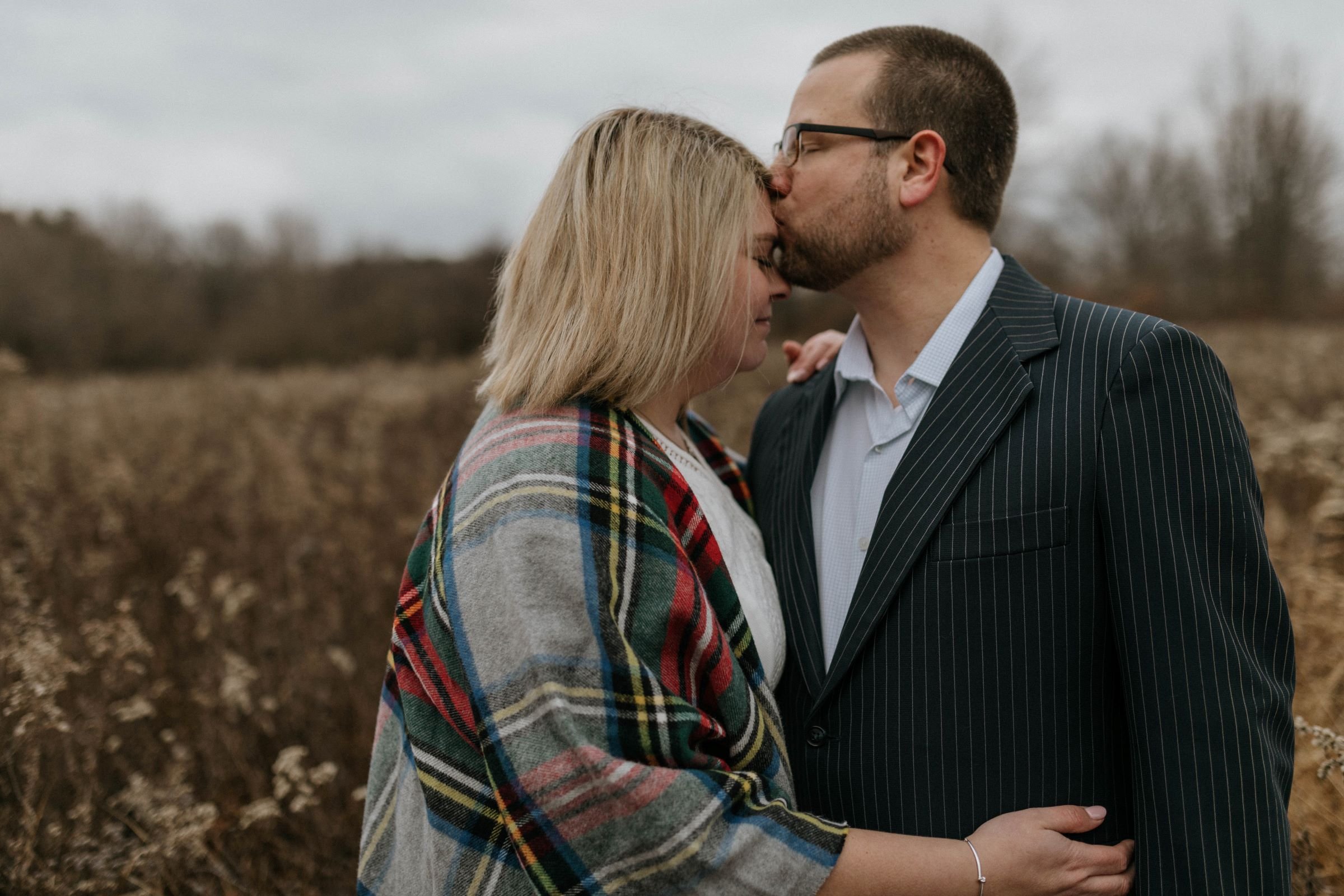 A husband kissing his wife's forehead during an elopement session in a field at the Montour Preserve.