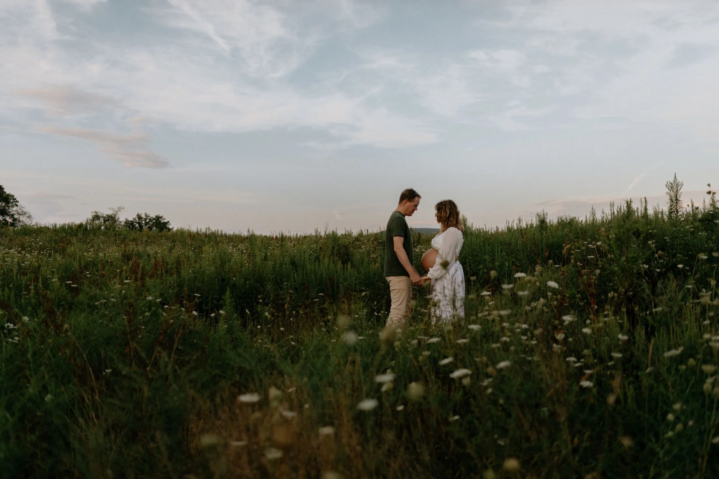 maternity session with a couple holding hands in a field of flowers in central Pennsylvania