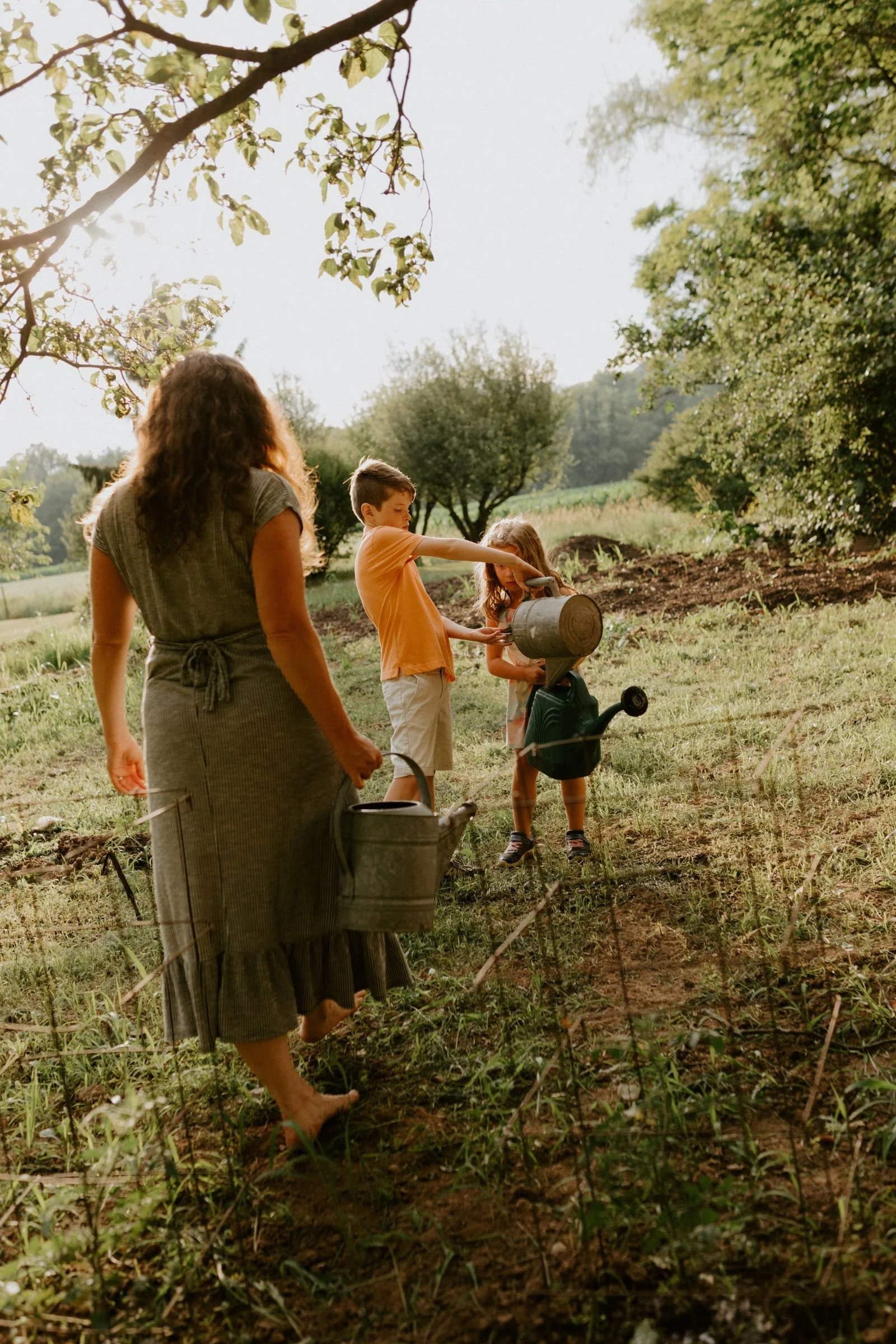 A woman walking with a young girl and boy with watering cans in the garden during their family session in Hughesville, PA.