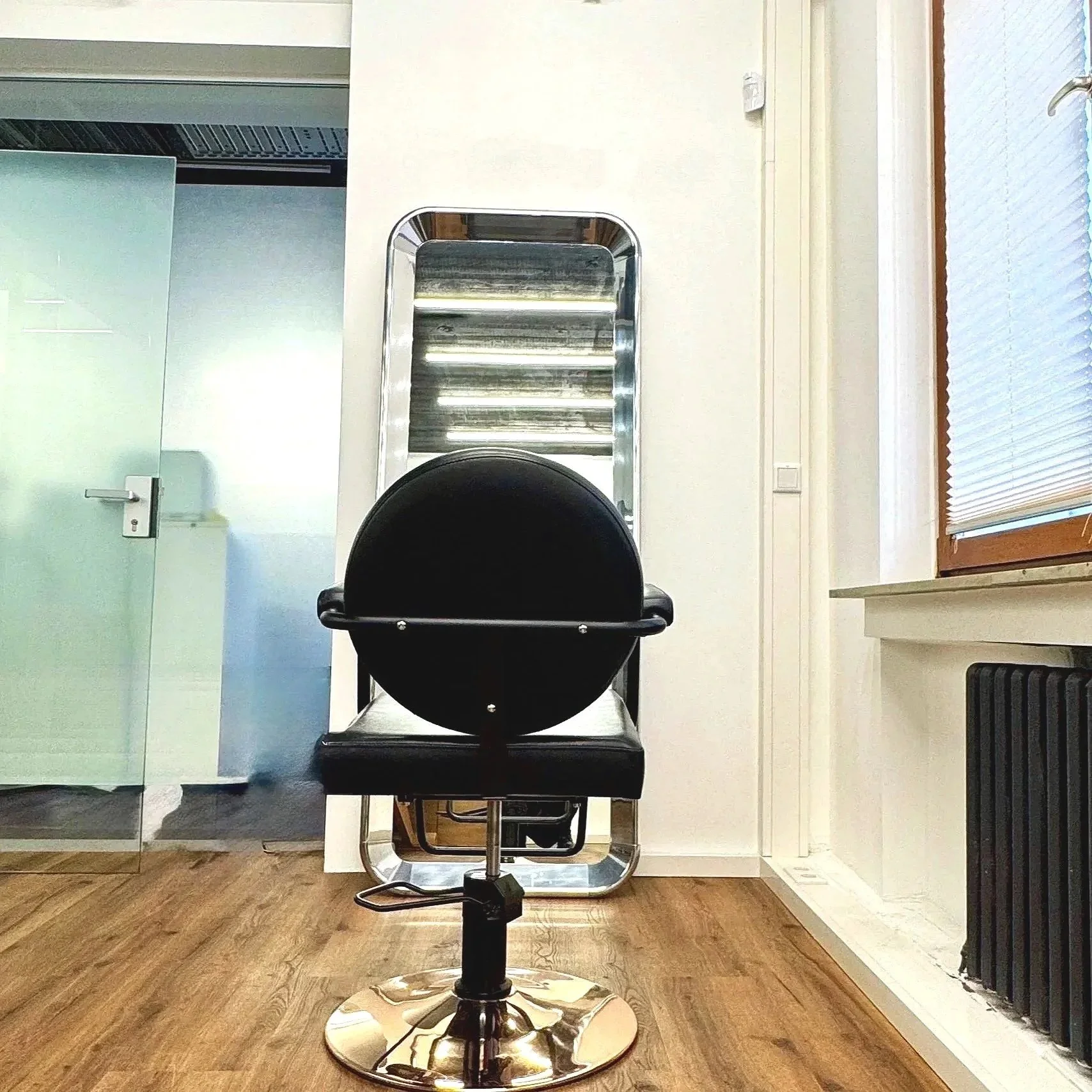 Minimalistischer Tiny Salon für Hair Professionals.
Klarer Spiegel, schwarzer Stylingstuhl und warme Materialien schaffen eine ruhige, konzentrierte Atmosphäre.