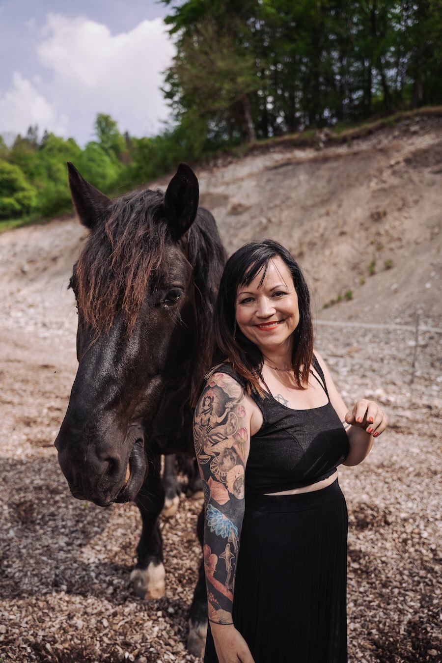 Alina, Tierkommunikatorin und Ausbilderin, steht mit schwarzem Pferd auf einer Koppel