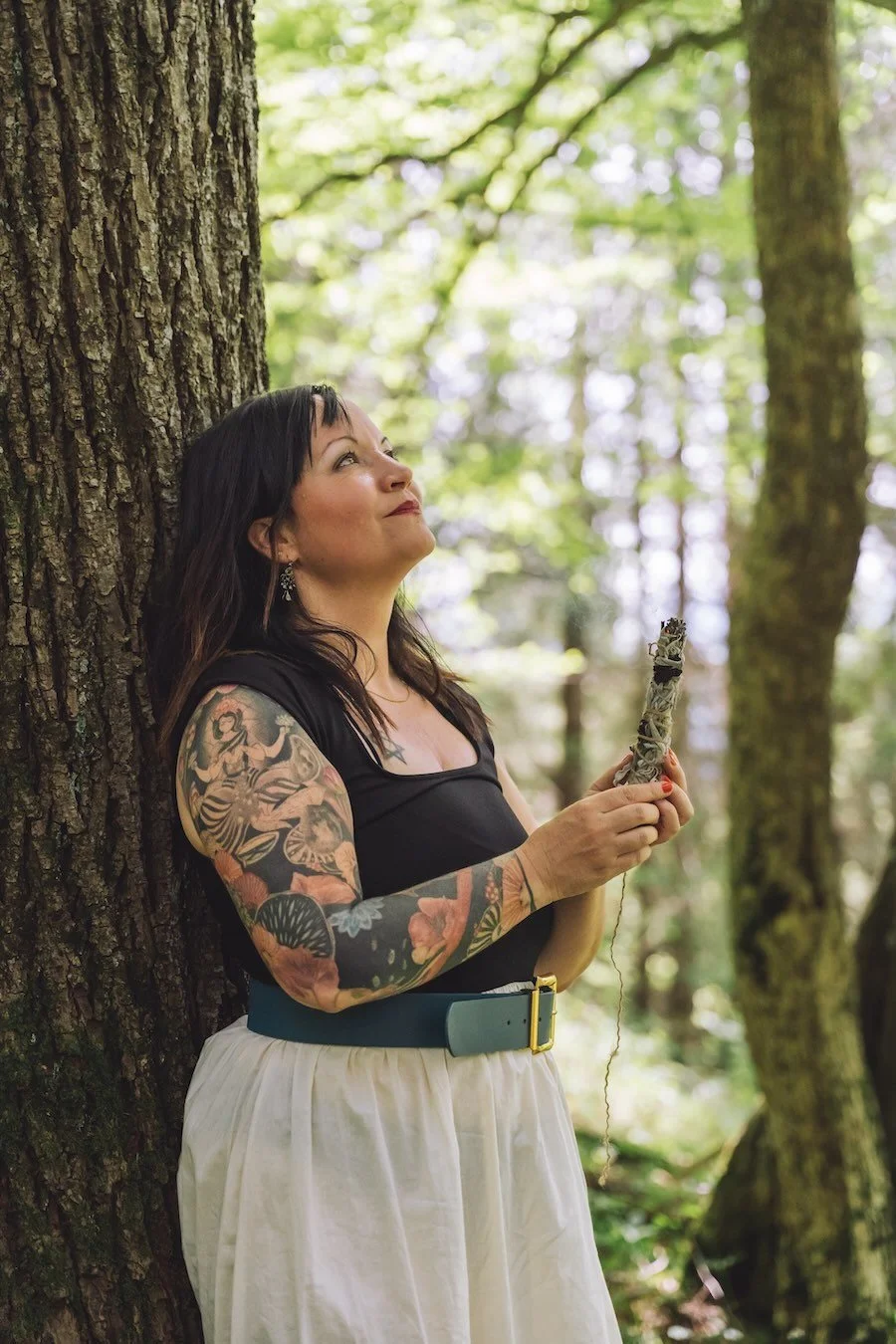 Tierkommunikatorin Alina lehnt im Wald an einem Baum.