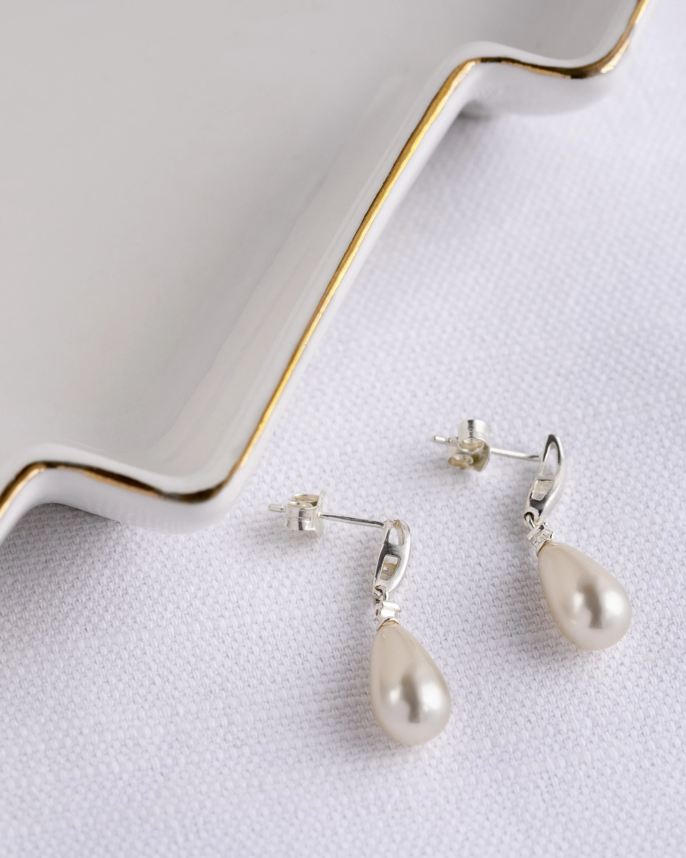 Elegant silver and pearl earrings styled with white with gold trim jewellery dish.