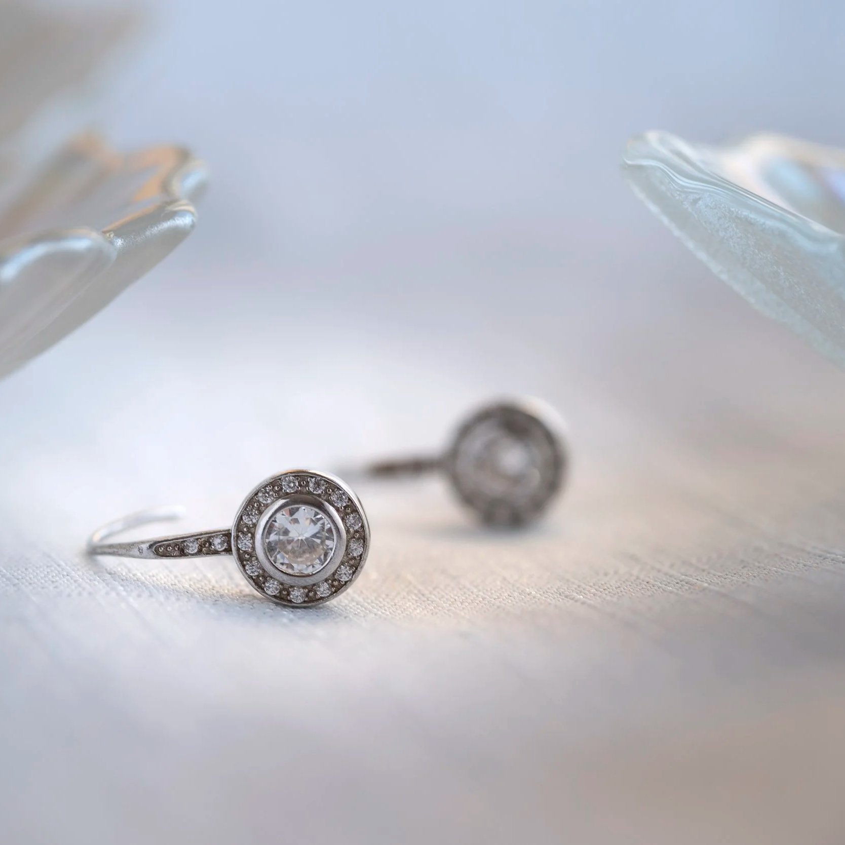 Silver earrings with large central diamonds, surrounded by smaller diamonds, resting on white fabric.