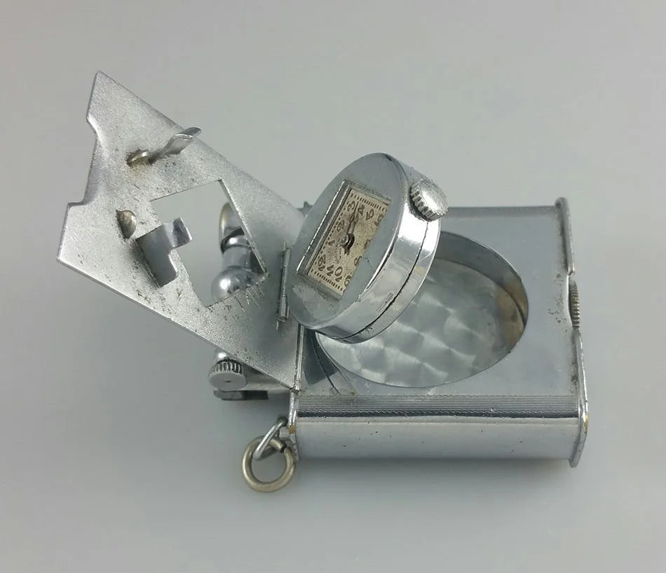 A vintage metal inspection tool with a built-in dial gauge and magnifying glass, used for precise measurements.