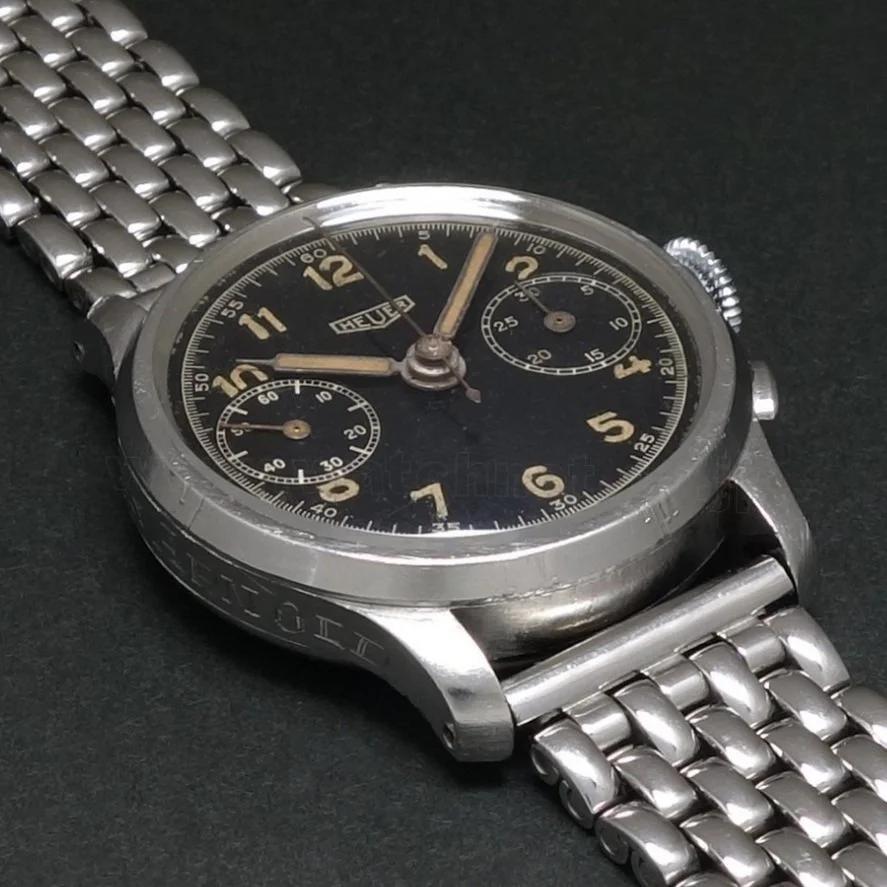A vintage Tag Heuer chronograph wristwatch with a black dial, gold numerals, and a stainless steel bracelet.