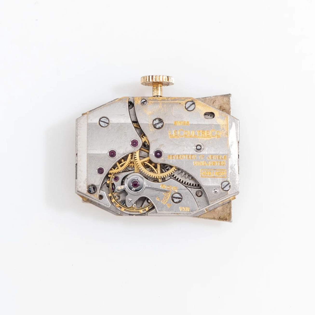 Close-up of a vintage watch movement with gears and screws, labeled with brand name Le Coultre, 17 jewels, and other specifications.