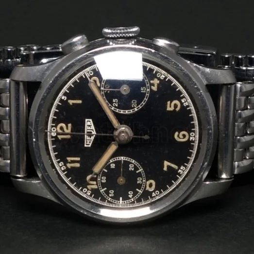 A vintage TAG Heuer chronograph wristwatch with a black dial, silver case, and metal bracelet, featuring multiple subdials and a tachymeter scale.