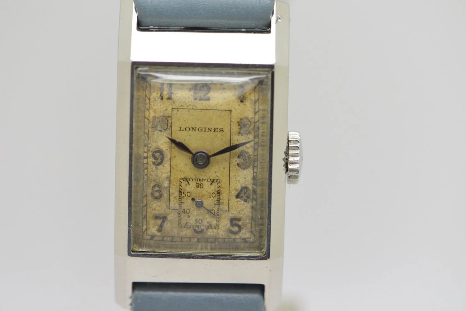 A vintage Longines wristwatch with a rectangular face, showing the time as approximately 9:14, featuring a smaller seconds subdial at the 6 o'clock position and a worn yellowish dial.