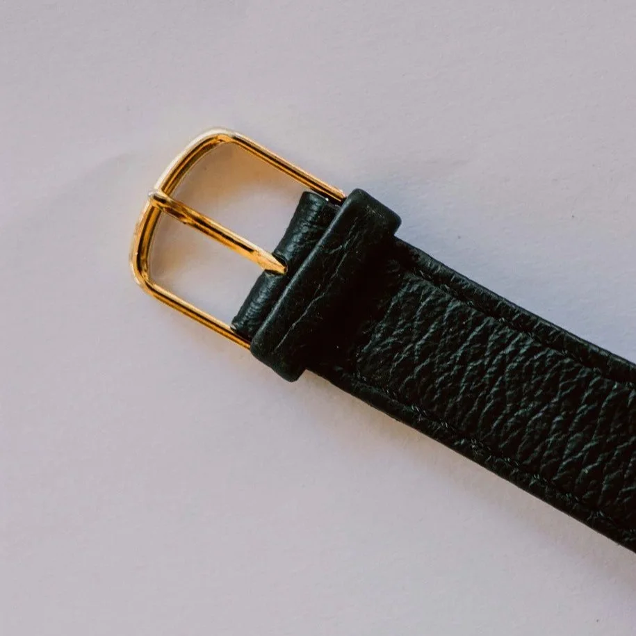 Close-up of a black leather belt with a gold buckle on a white background.
