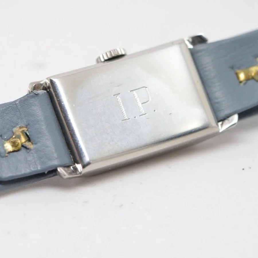 A silver wristwatch with a gray leather strap, engraved with the letter P on the back.