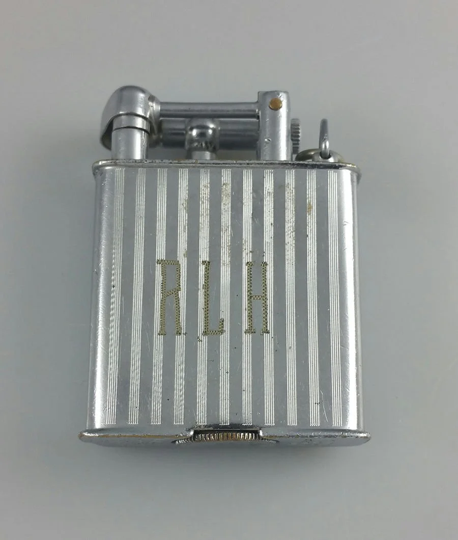 A vintage silver lighter with a ribbed design and the word 'ALOH' engraved on the front.