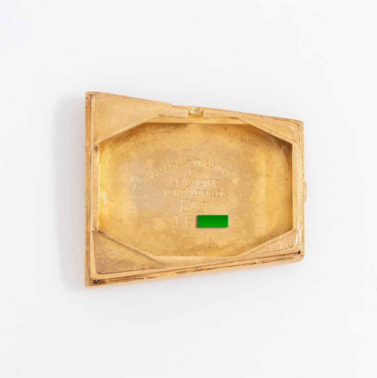 Gold-colored vintage compact with embossed text inside and a small green tab.