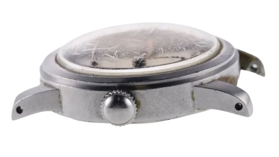 Close-up of a worn vintage men's wristwatch with a scratched glass face and metal casing