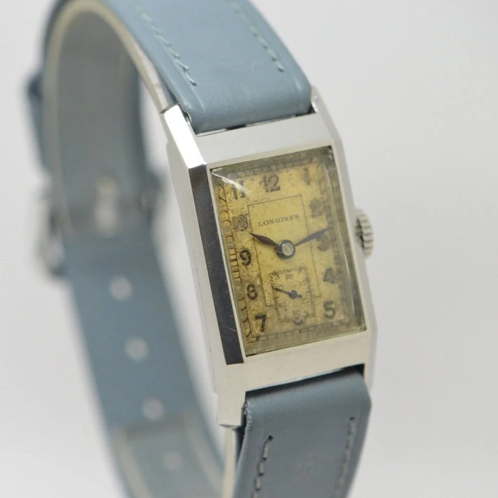 Vintage rectangular wristwatch with a yellowed dial, black numerals, and a gray leather strap.