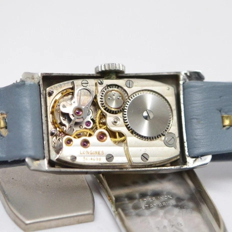 Close-up of an open vintage Longines wristwatch showing its mechanical inner workings and gears, with a light blue leather strap.