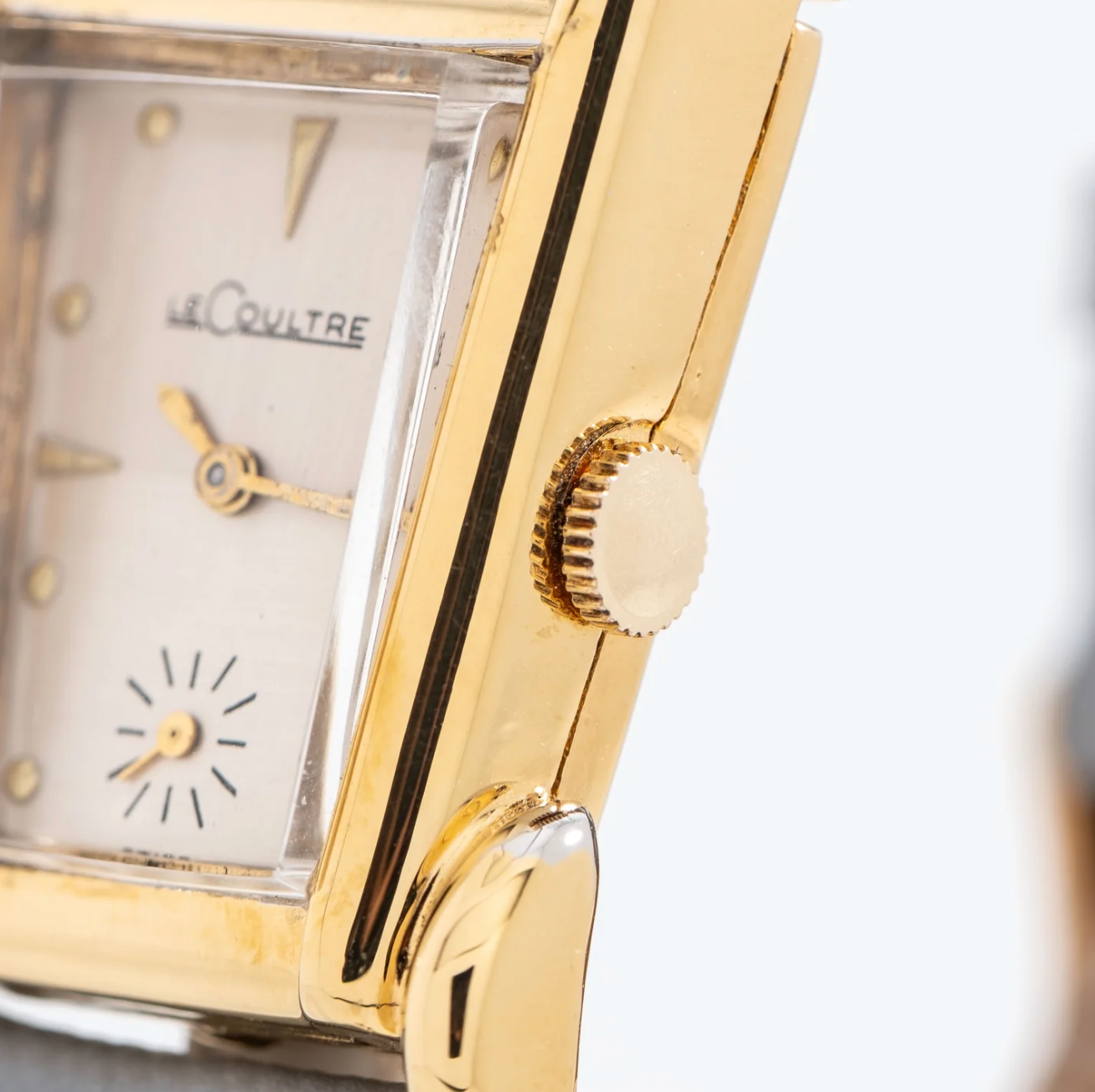 Close-up of a vintage gold-tone wristwatch with a rectangular face, showing the brand name 'LeCULTRE' and a small seconds subdial at the 6 o'clock position.