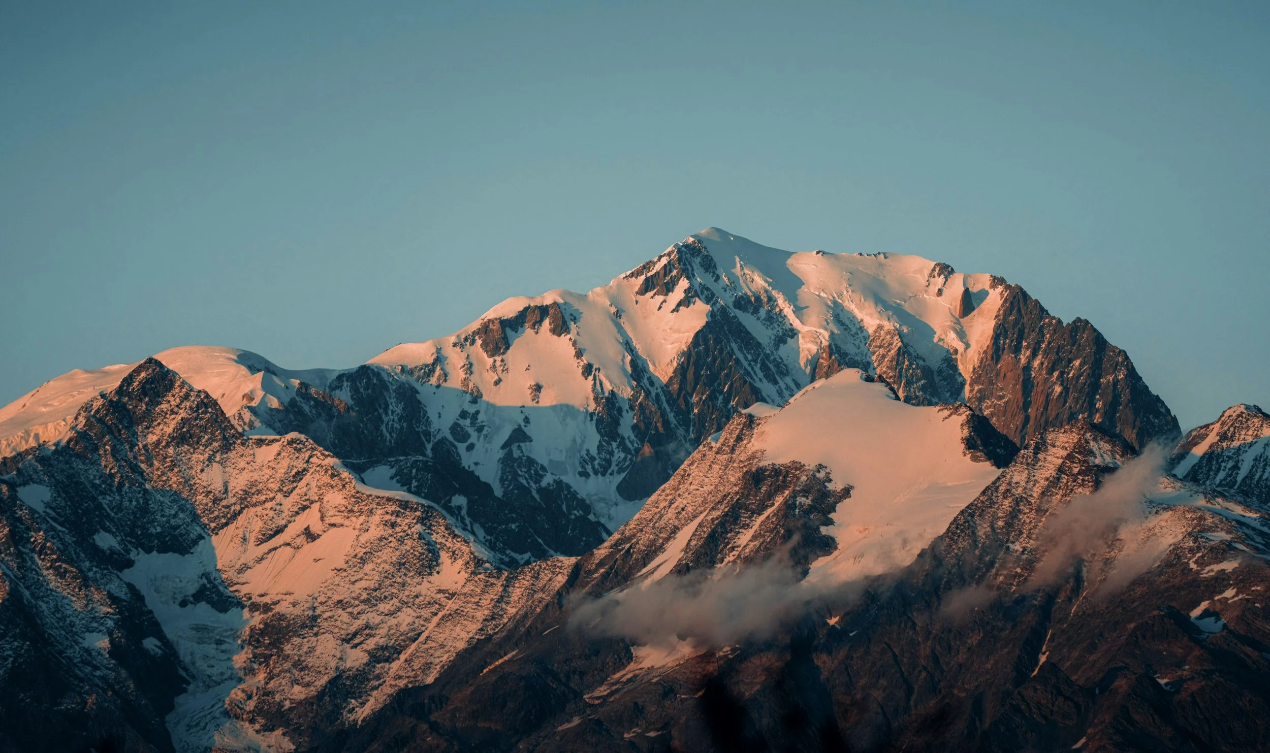 Snow-covered mountain peaks at sunset with clear blue sky.