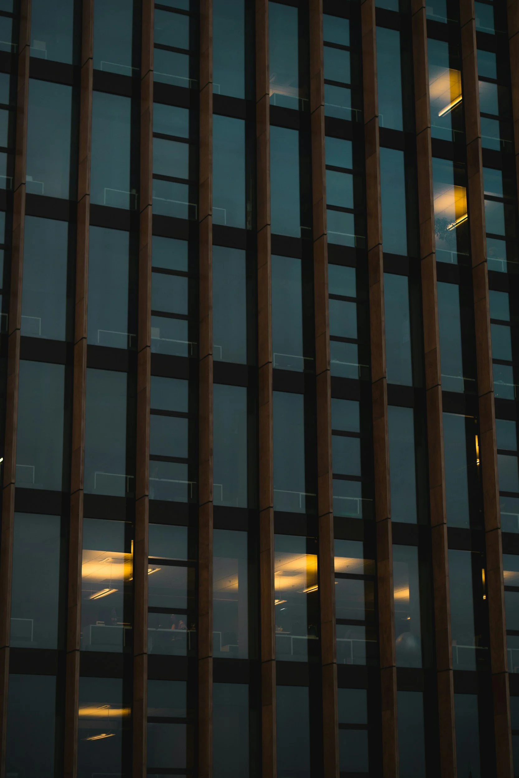 Close-up of a modern building's exterior with vertical wooden slats and glass windows, some illuminated from inside.