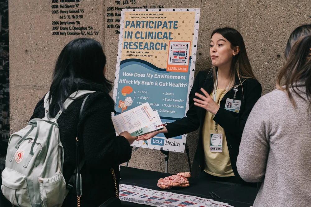 Attendees talk with an exhibitor beside a clinical research poster