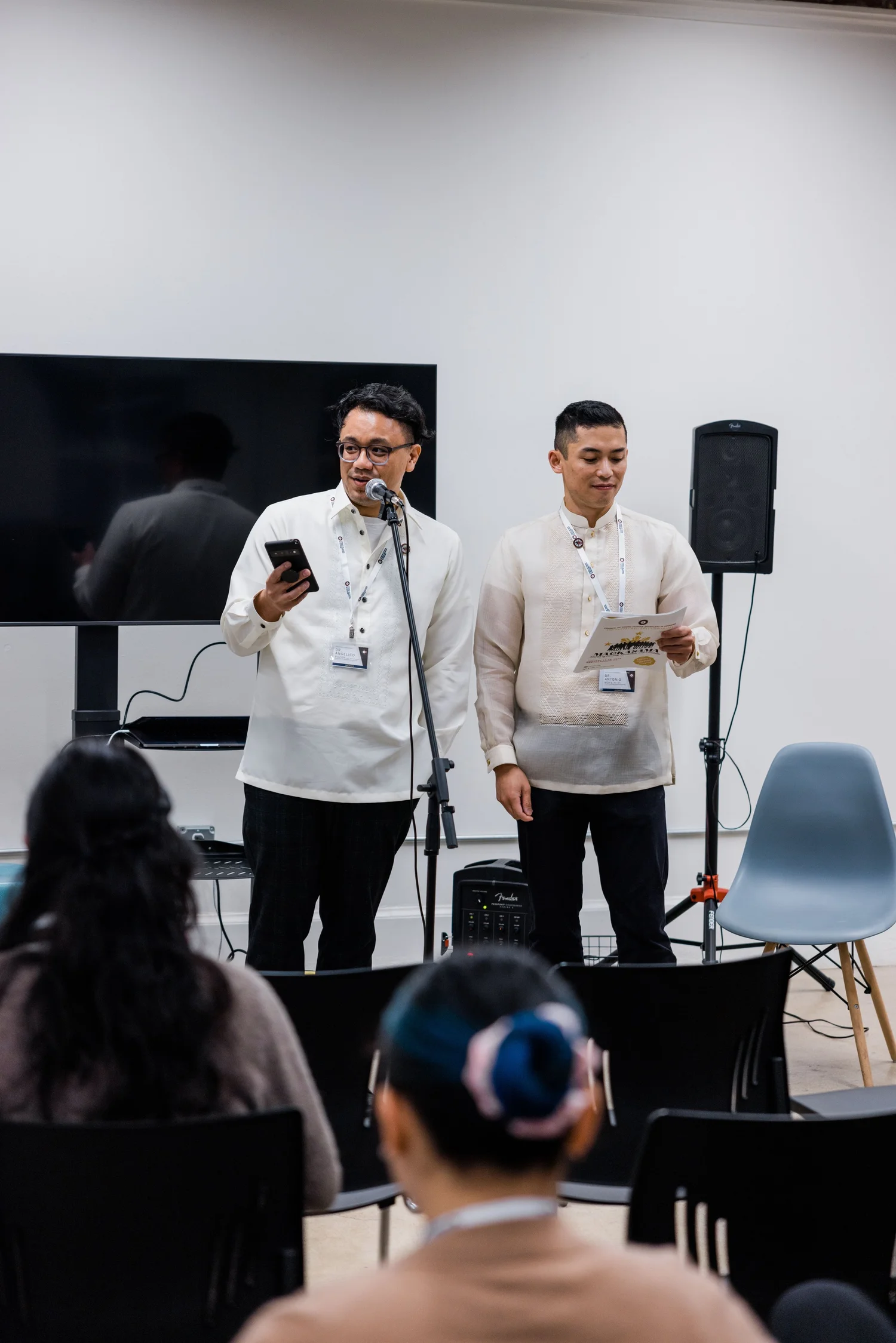 Two CYFAM leaders in barong tagalog speak at a microphone during a CYFAM event.
