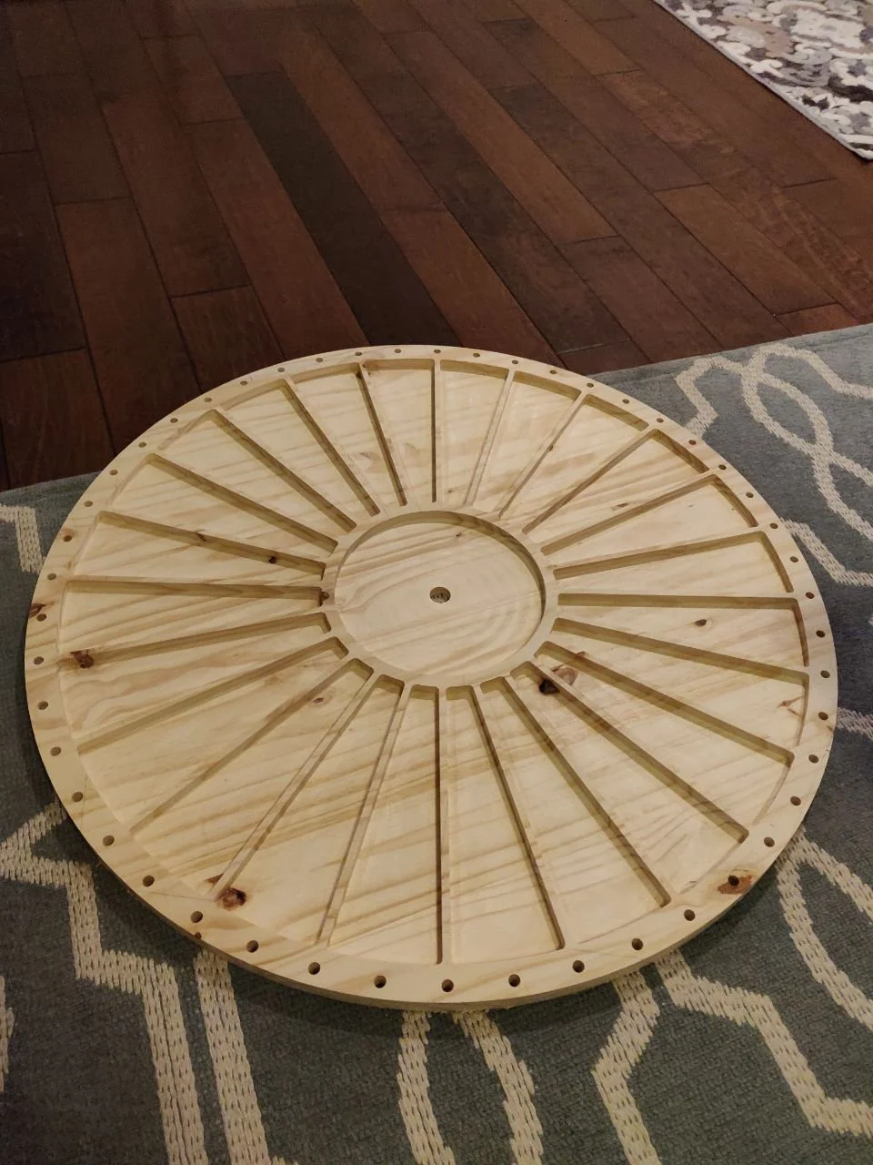 Round piece of plywood with holes and radial wedges carved into it, fresh off the CNC router.