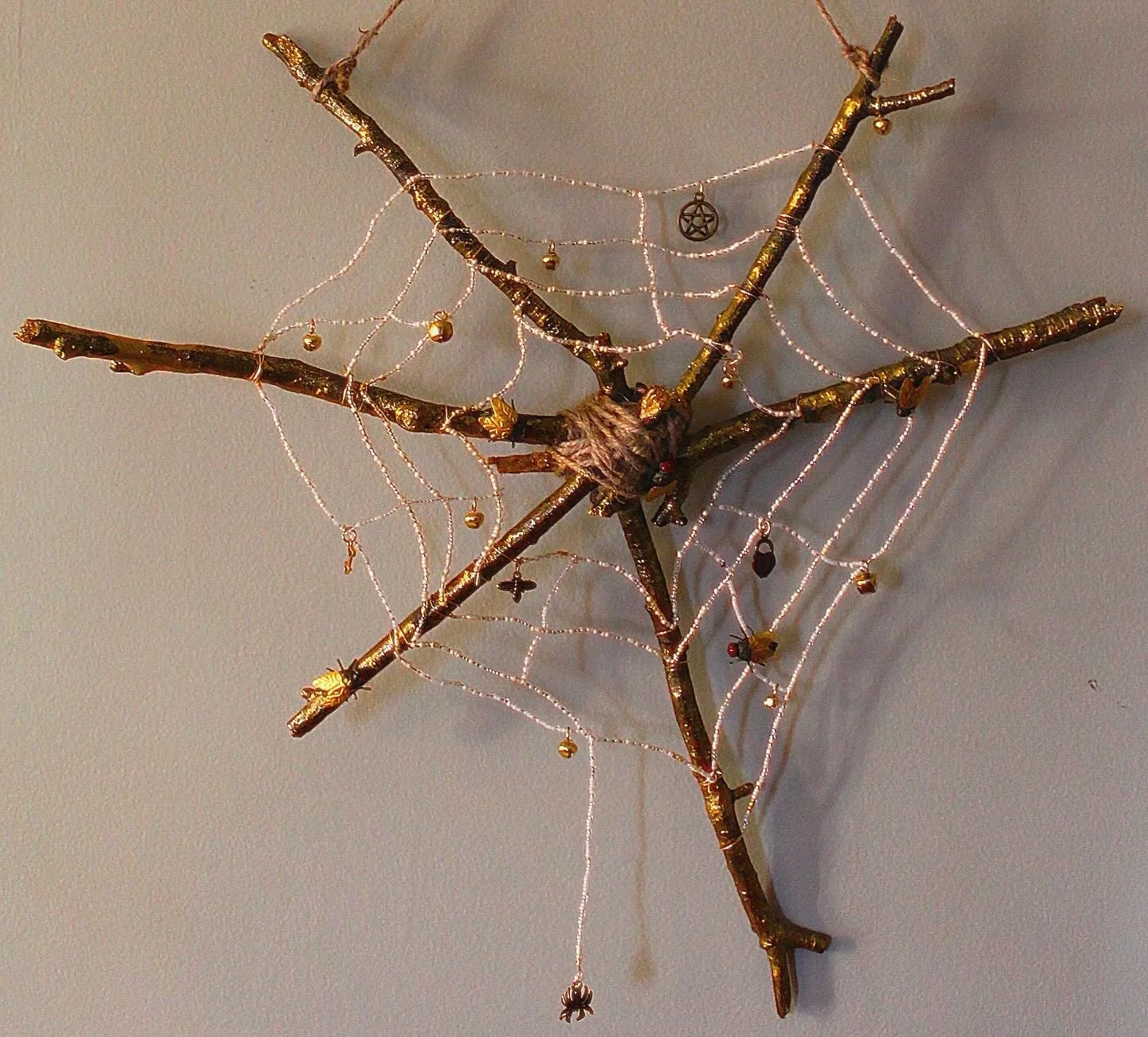 A wall decoration made of intertwined branches decorated with spiders and a small pentagram charm, resembling a spooky or Halloween-themed ornament.