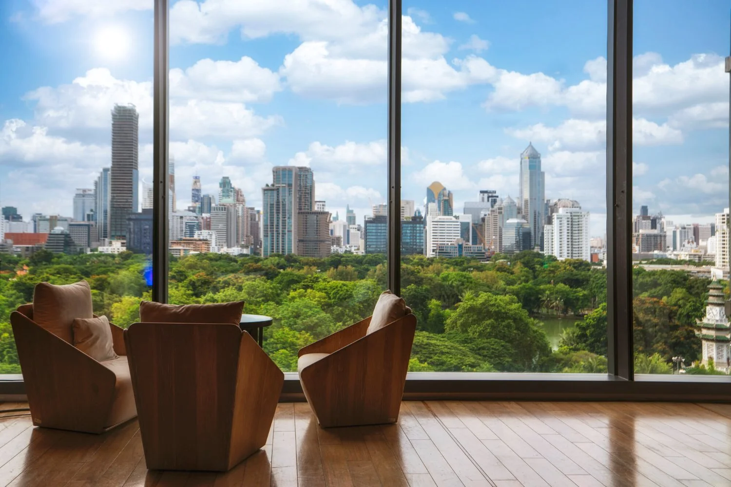 Modern living room with large floor-to-ceiling windows overlooking a city skyline with tall buildings and a green park in the foreground.