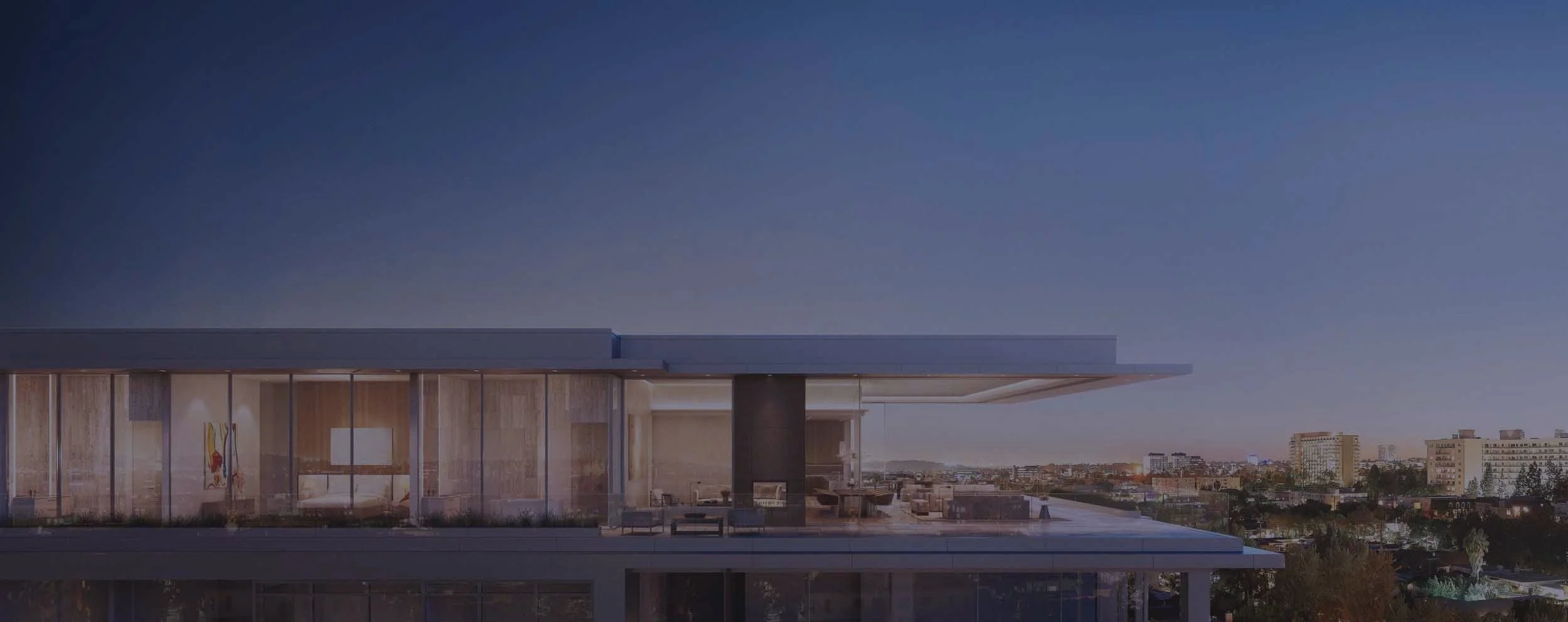 Modern building with large glass windows and rooftop patio, city skyline in the background during dusk.