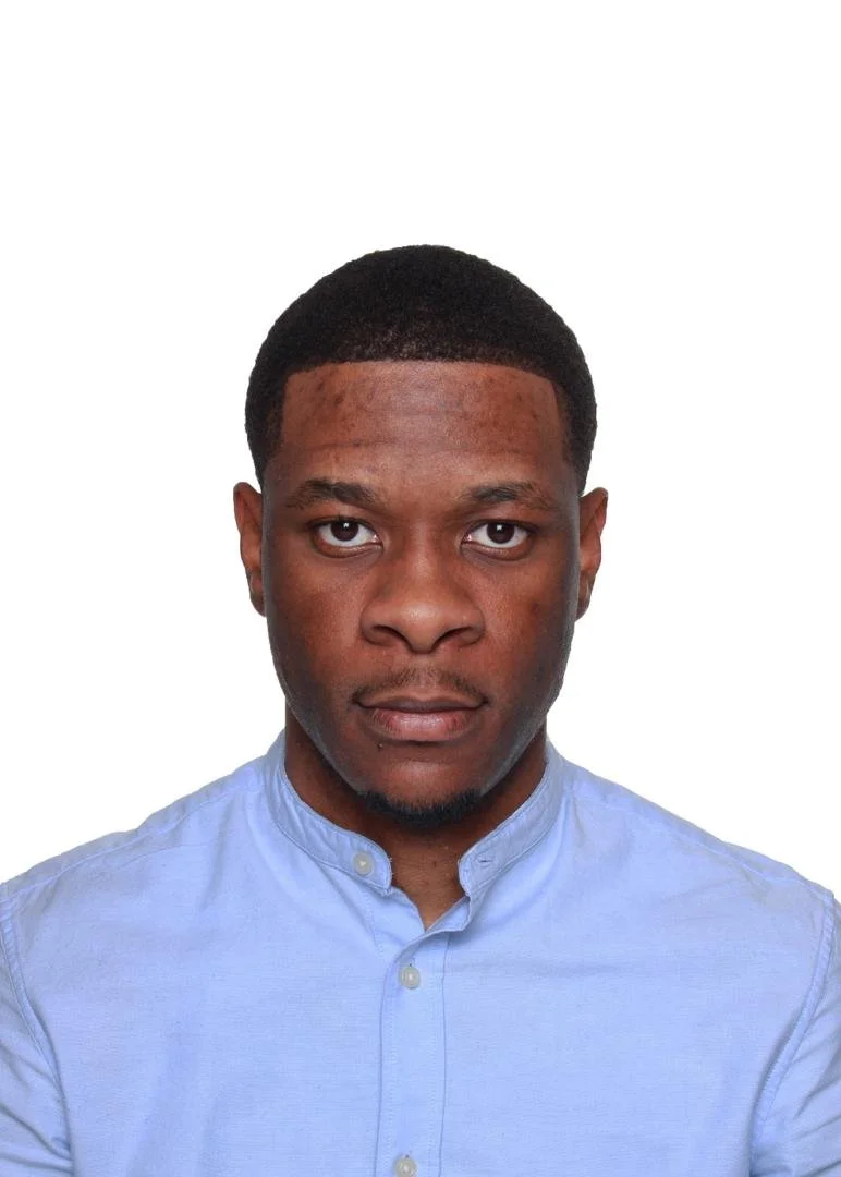 Headshot of a young man with short hair, wearing a light blue collared shirt, looking directly at the camera against a plain white background.