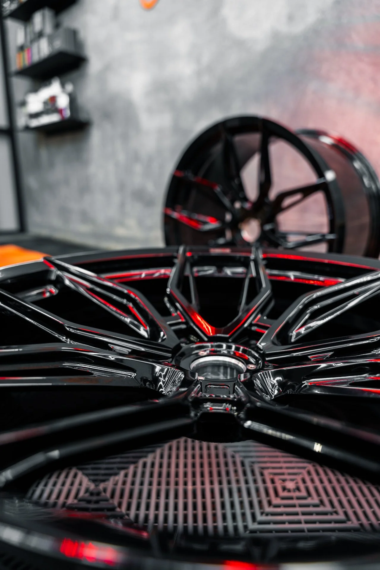 Close-up of a black alloy wheel with red accents, in a workshop or garage with a concrete wall background.