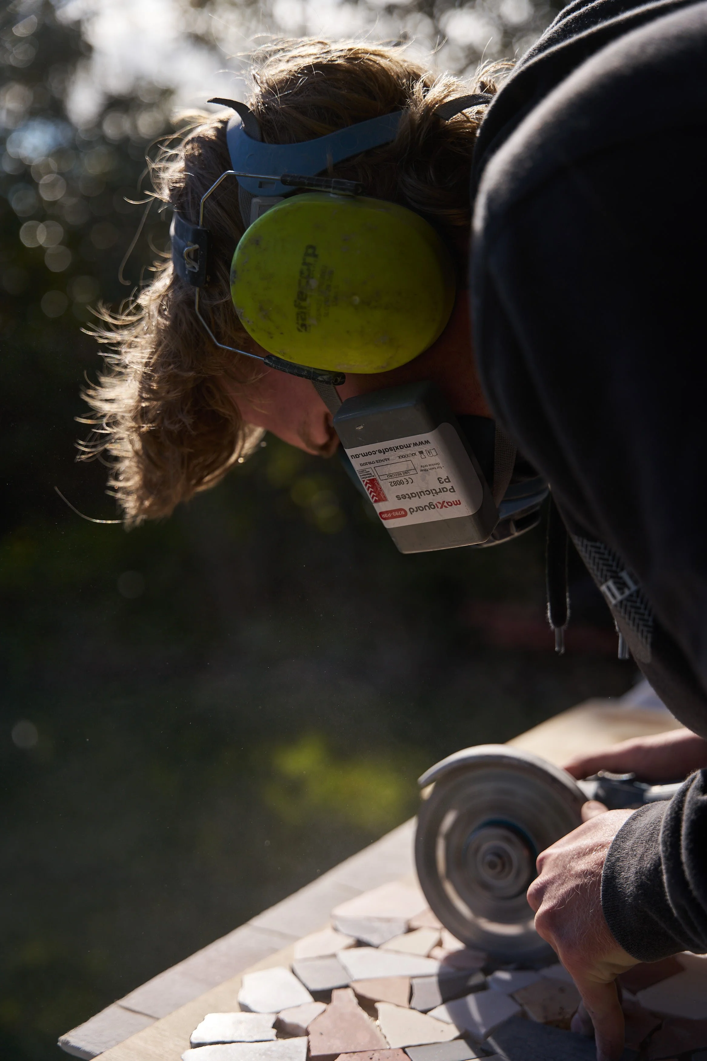 Close-up of a person using a circular saw to cut stone tiles outdoors, with a focus on their hands and the saw.