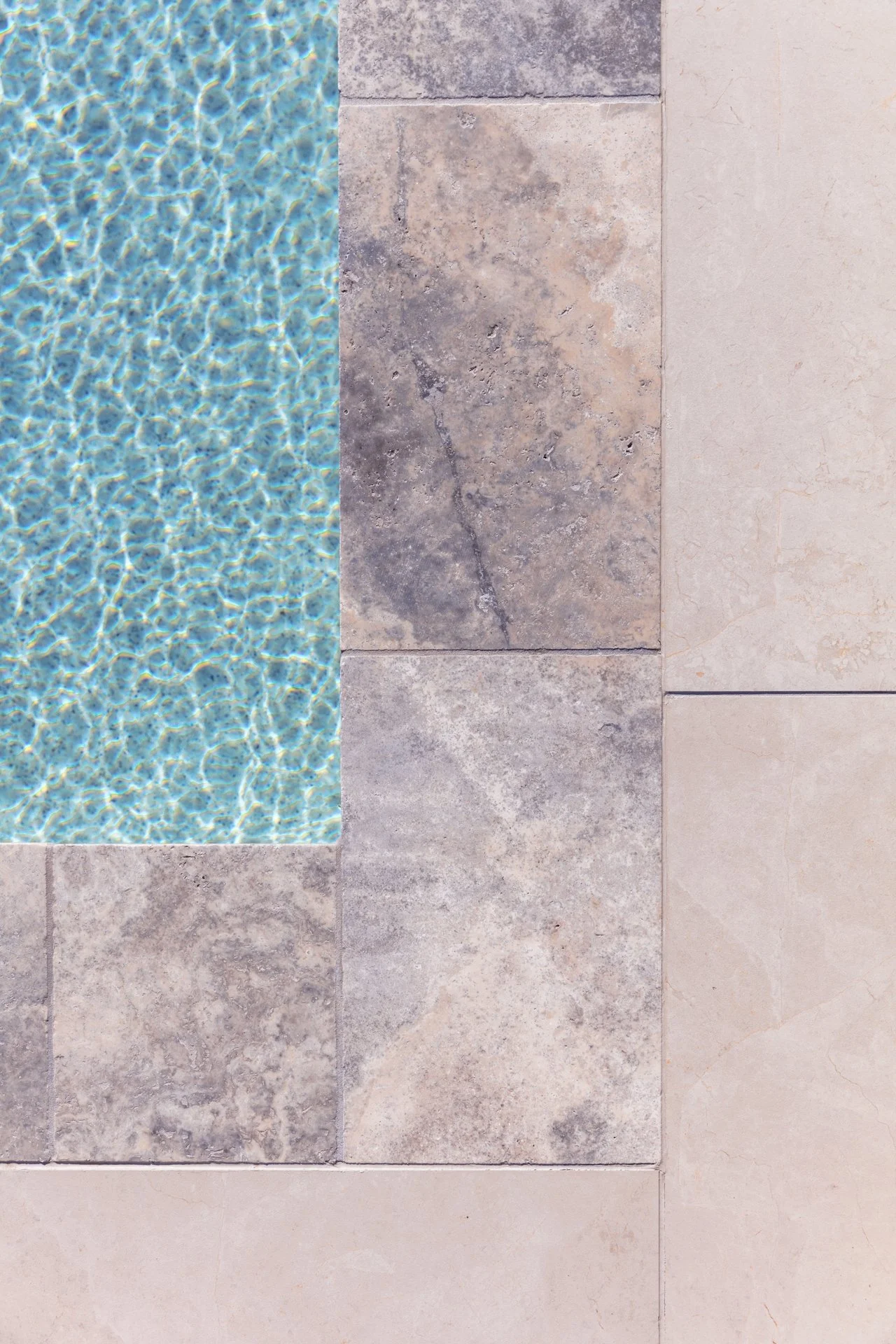 Close-up of a tiled surface with different types of tiles, including a section of a swimming pool with water, various stone tiles, and cream-colored tiles.