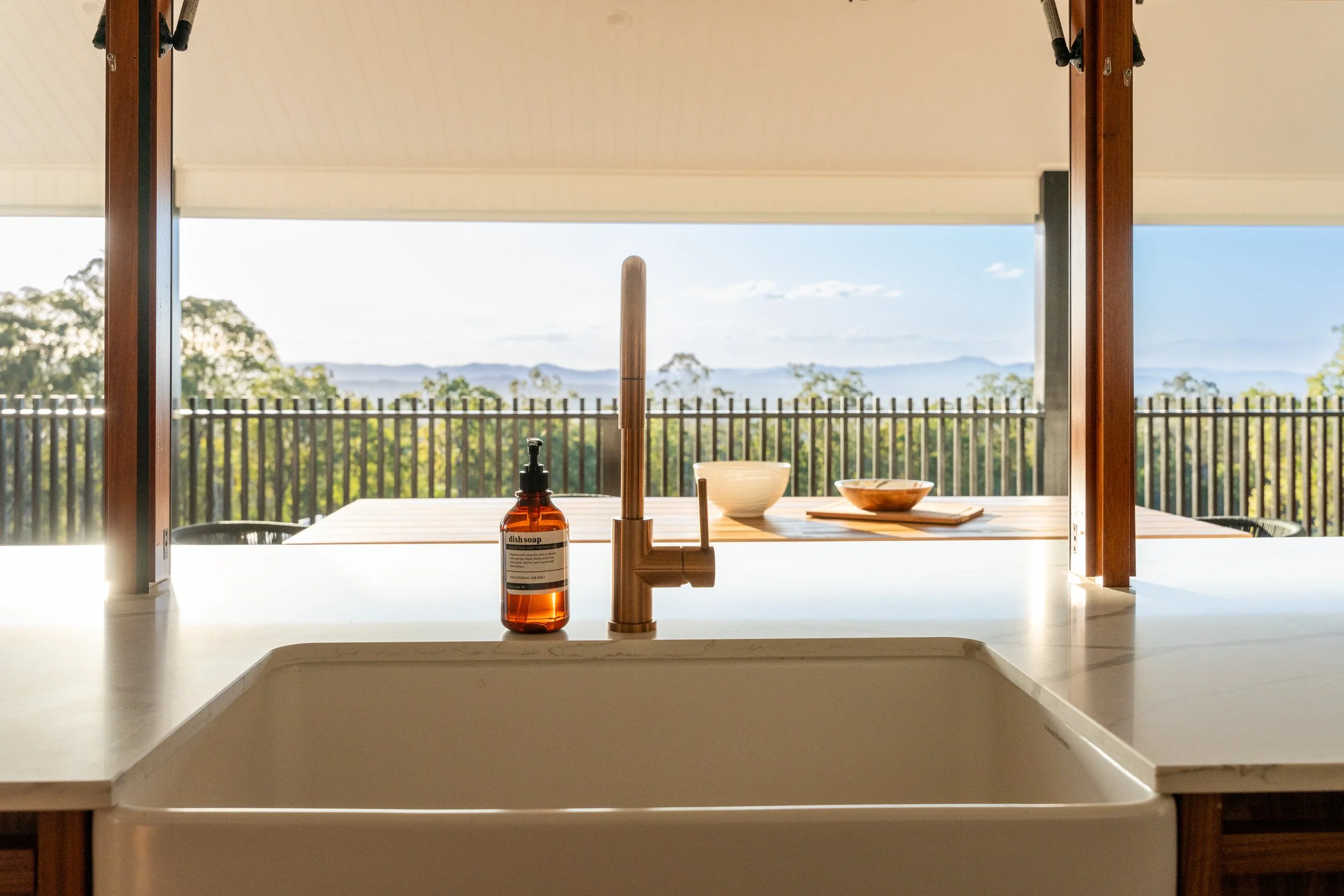 Kitchen sink with a soap dispenser, view of a window with a landscape of trees and mountains, bowls on the counter.