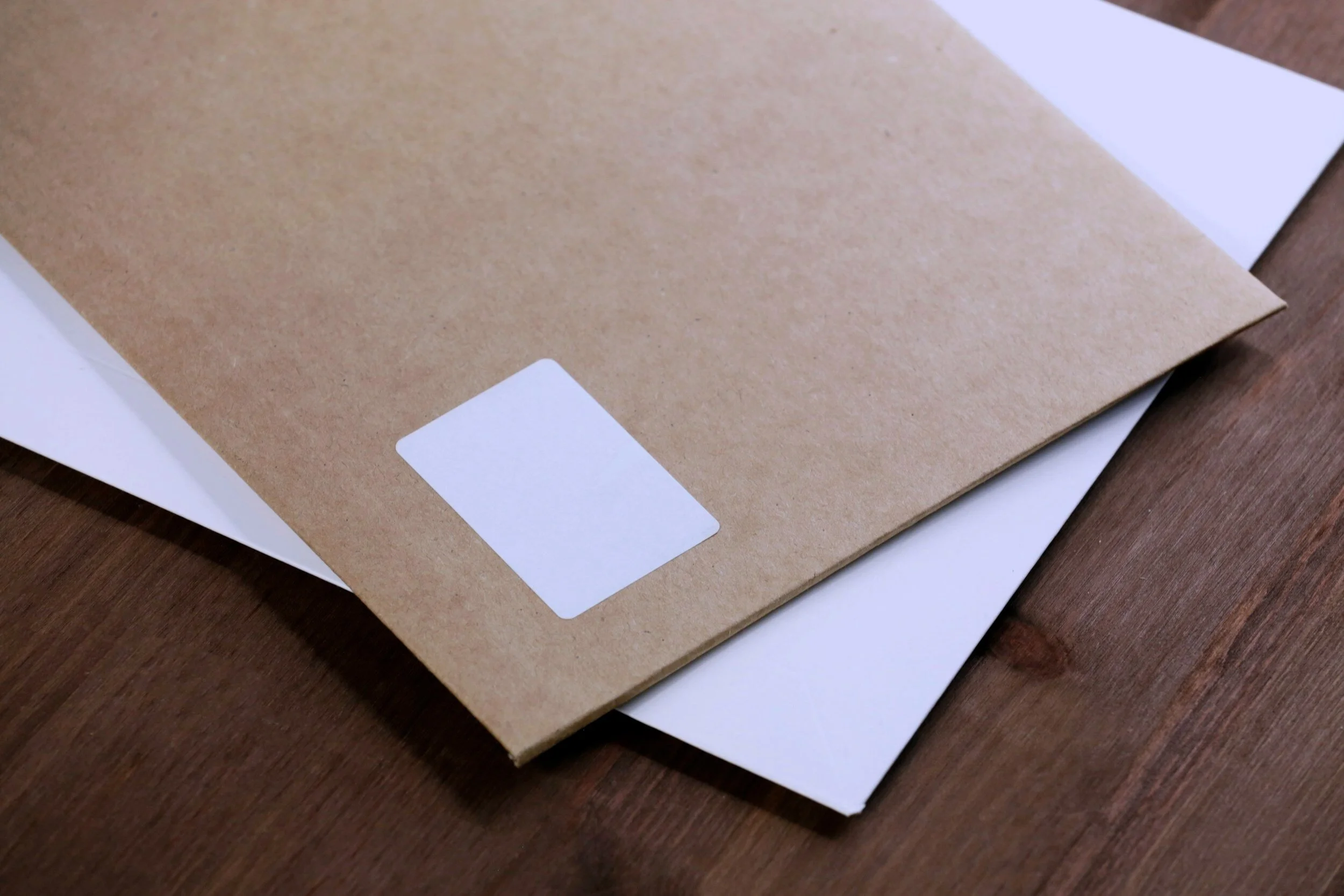 Brown envelope with a white sticker on a white envelope, placed on a wooden surface.