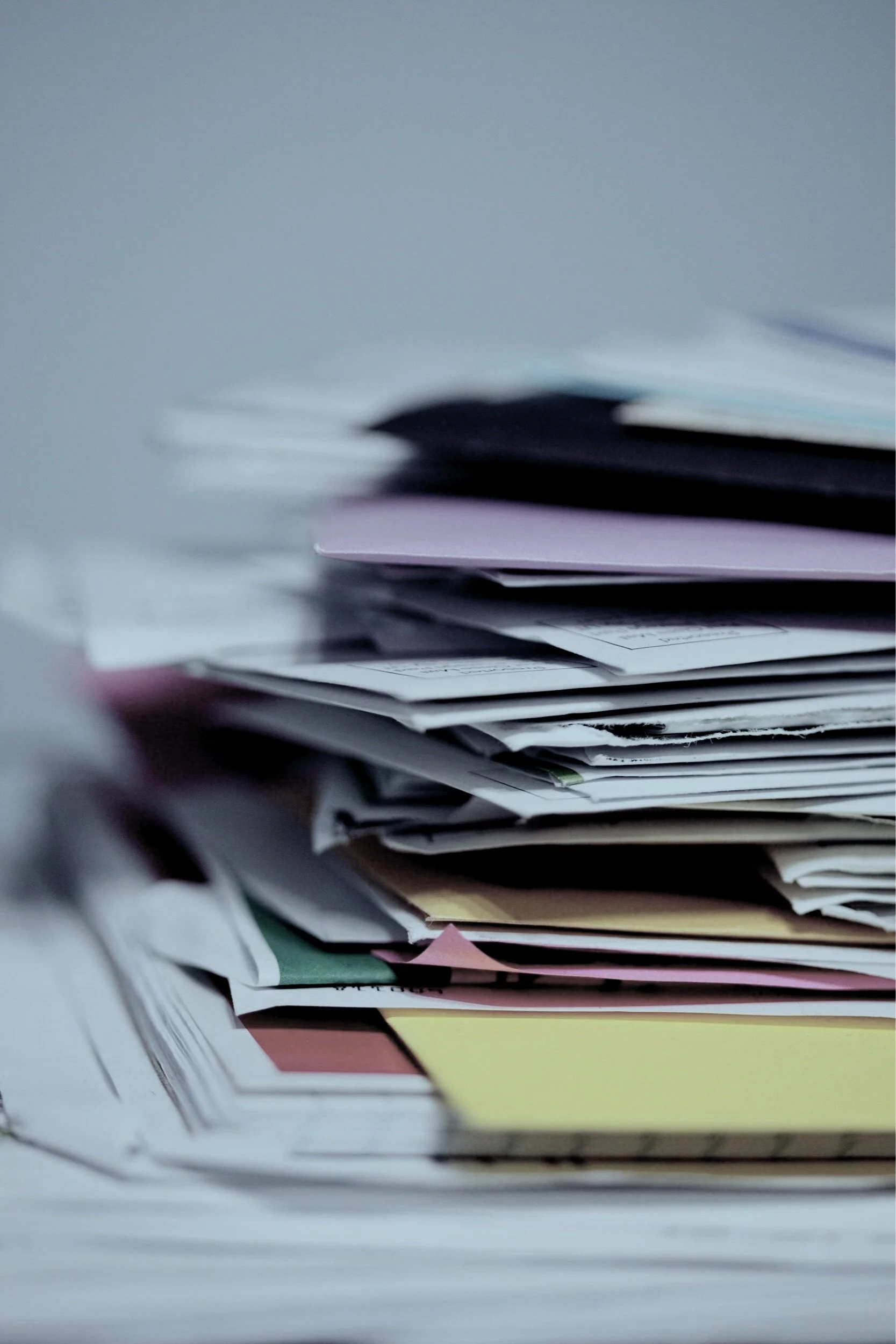 A close-up of a cluttered stack of paperwork and files, with various papers and folders overlapping.