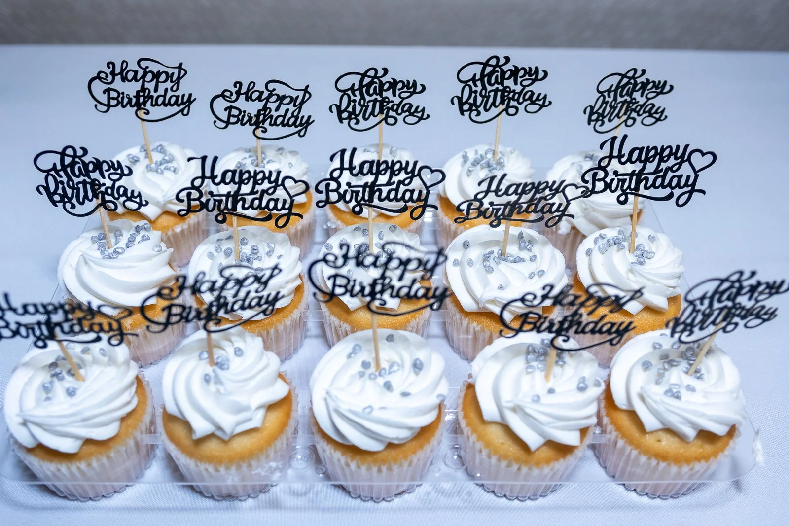 Tray of cupcakes decorated with white frosting, silver sprinkles, and 