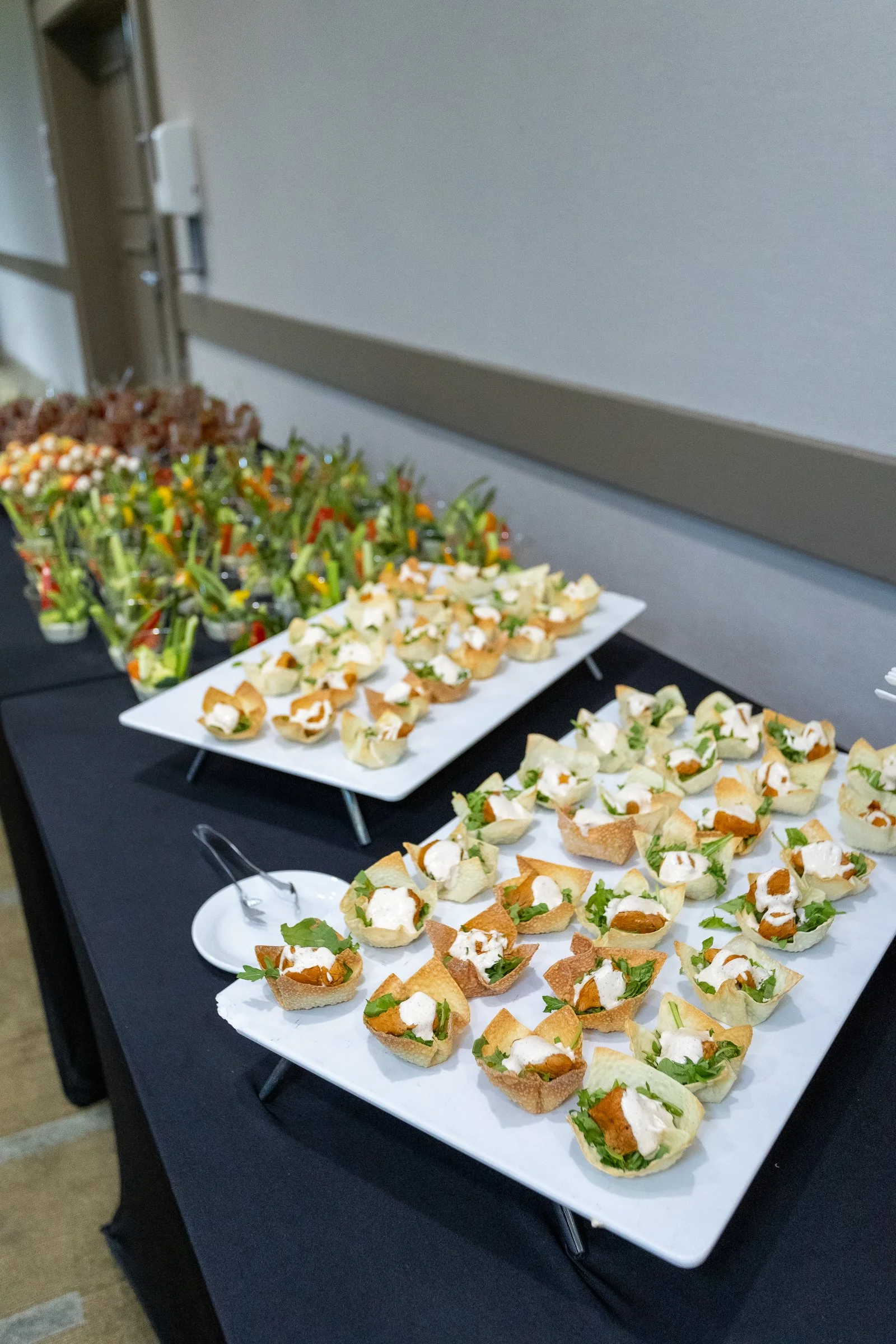 Assorted appetizers, including small sandwiches with greens and a white sauce, arranged on white trays for a catering event.