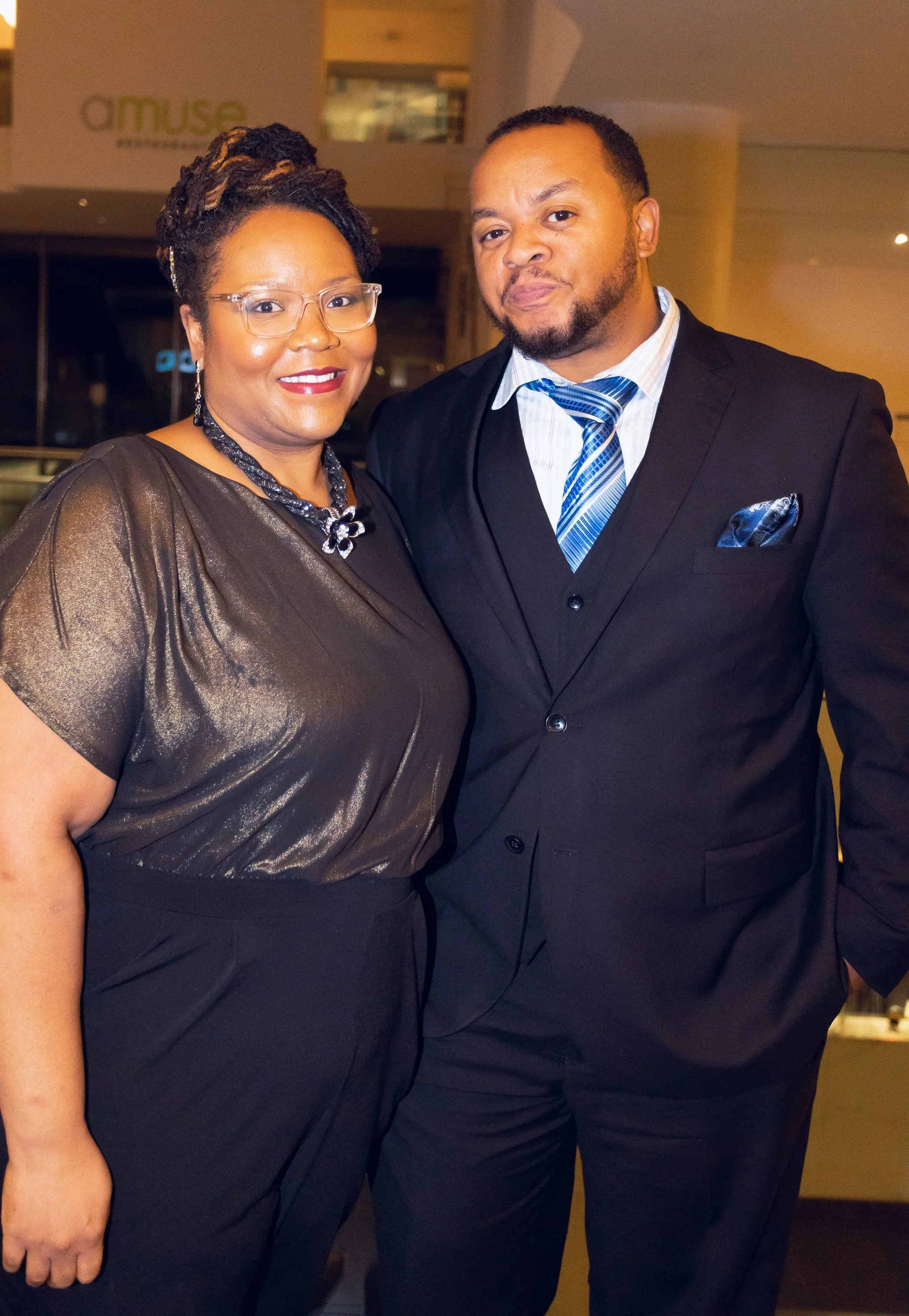 A woman and a man dressed in formal attire standing together at an indoor event.