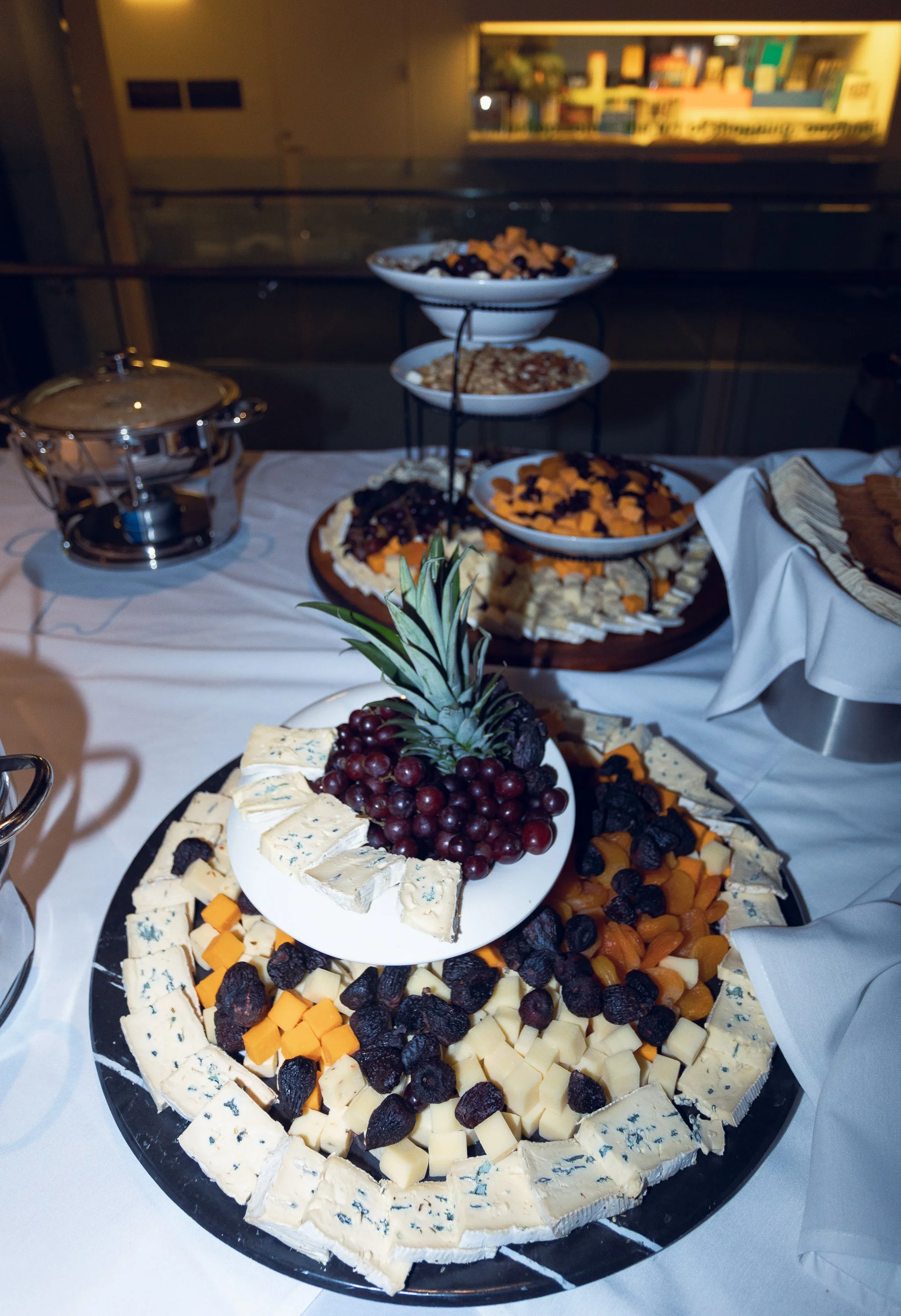 Cheese and fruit platter with grapes, dried fruit, and assorted cheeses on a black tray with a pineapple in the foreground.