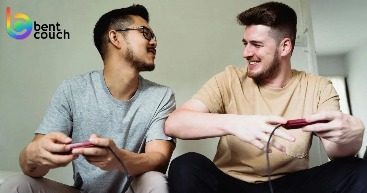 Two young men smiling and playing video games together with controllers, illustrating gaming, friendship, social connection and mental health benefits for gay and queer men.