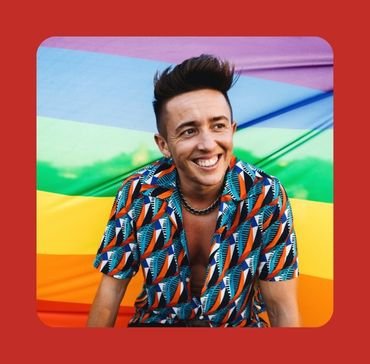 A smiling person standing in front of a rainbow flag, representing identity, self acceptance, and affirming identity counselling for gay, bisexual, queer, and LGBTQ+ men at Bent Couch.