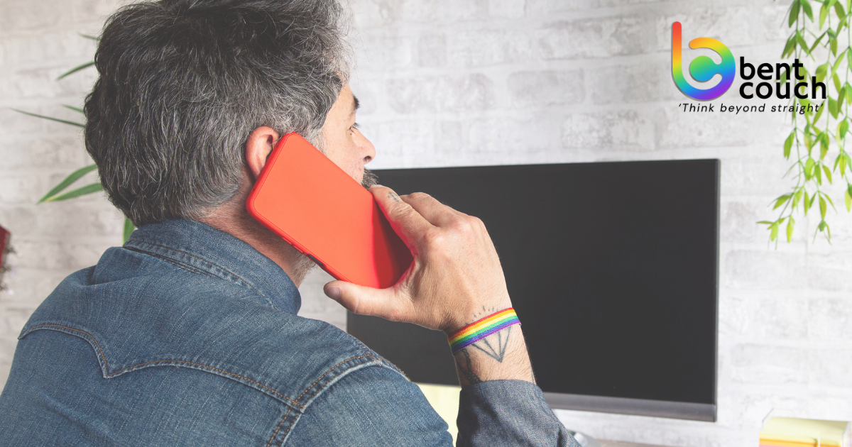 A man wearing a rainbow wristband speaks on his phone at home, representing free online counselling and mental health support options for gay and queer men across Australia.