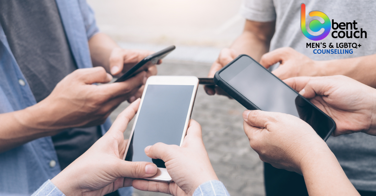 Several men standing together while each looks down at a smartphone, illustrating phone use, social disconnection, and its impact on gay men’s mental health and real world connection.