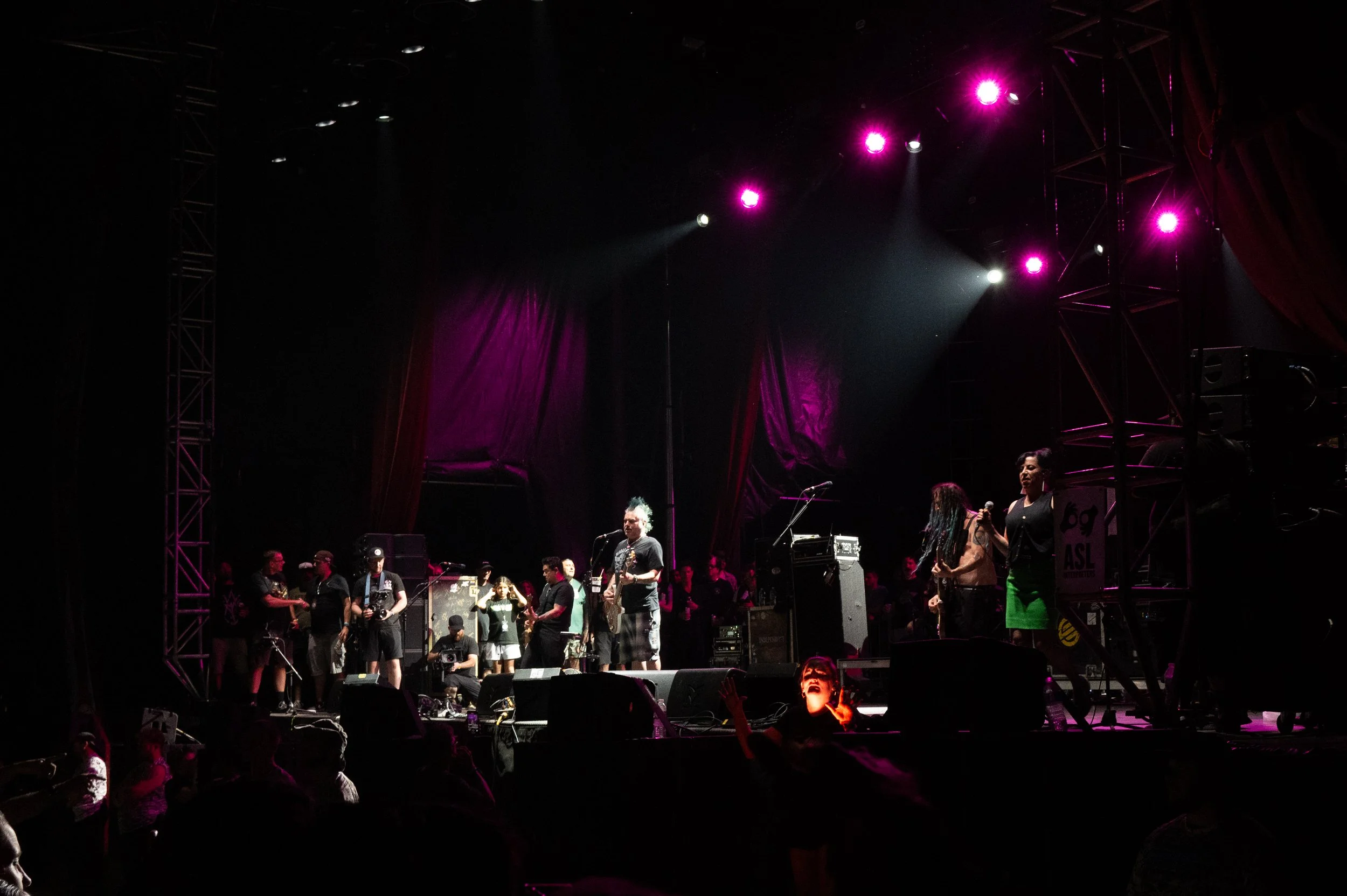 Band performing on stage with purple and white lighting at a concert.