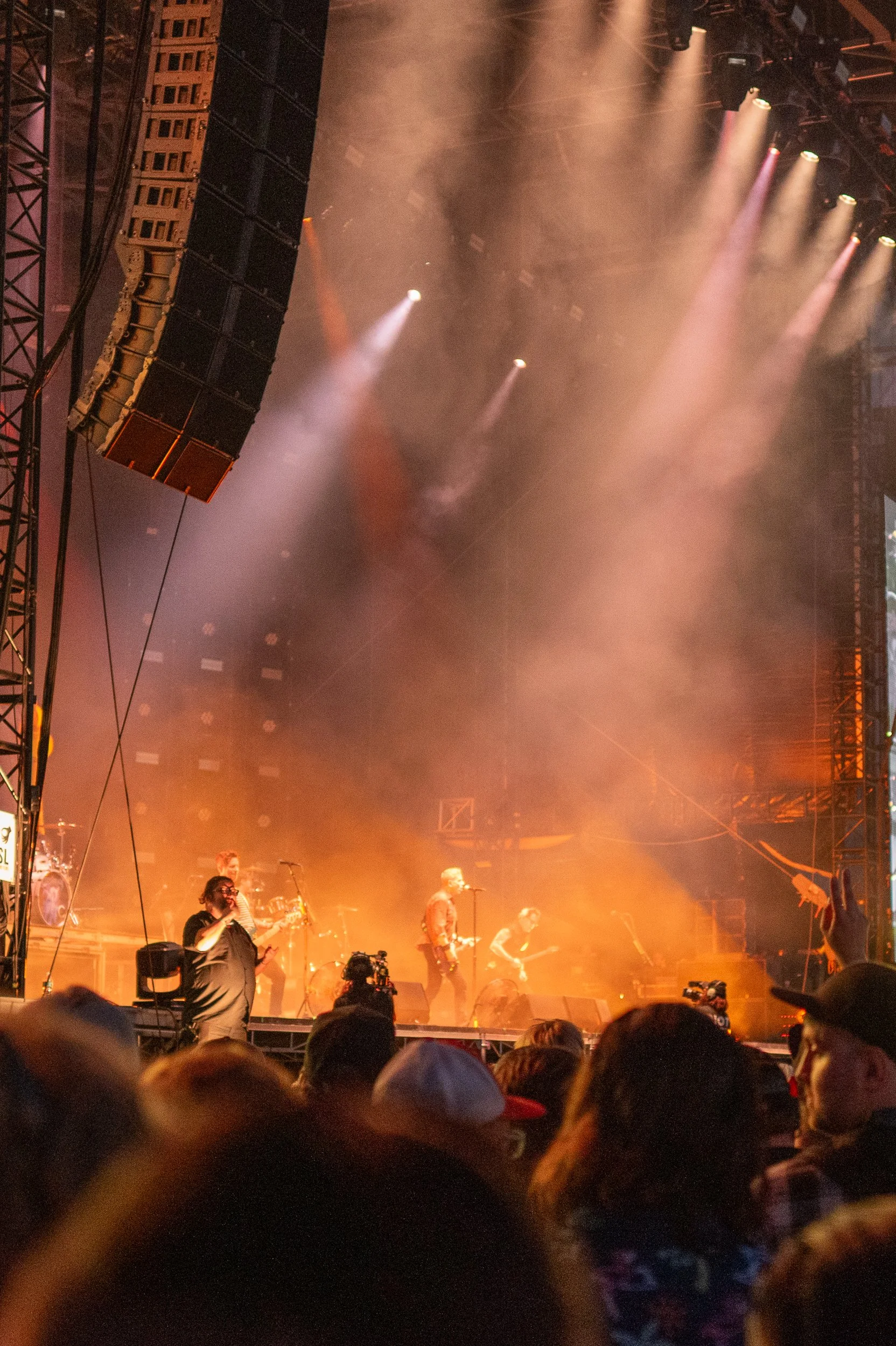 A live concert with a band performing on stage, illuminated by colorful stage lights and smoke, with an audience watching.
